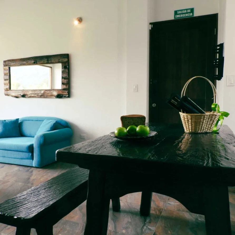 Interior de Casa Zuetana en Zipaquirá con sala y comedor rústicos, sofá azul y espejo de madera con reflejo natural.