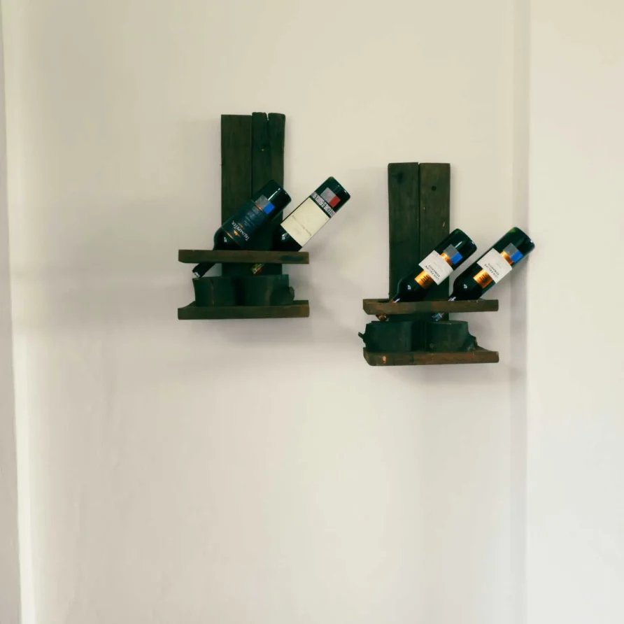 Dos estantes de vino rústicos de madera con botellas en pared blanca, decoración de Casa Zuetana en Zipaquirá.