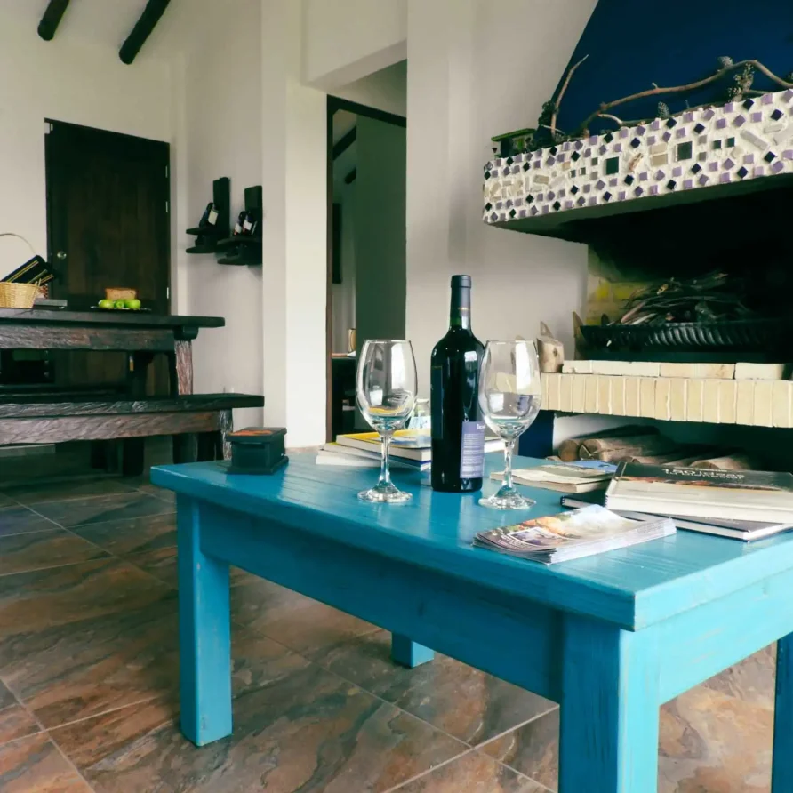 Sala rústica de Casa Zuetana en Zipaquirá con mesa azul, chimenea y vino. Ideal para alquiler vacacional bonito.