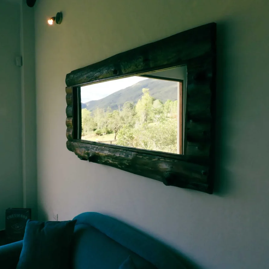 Espejo rústico con marco de madera reflejando un hermoso paisaje montañoso y verde en Casa Zuetana, Zipaquirá.