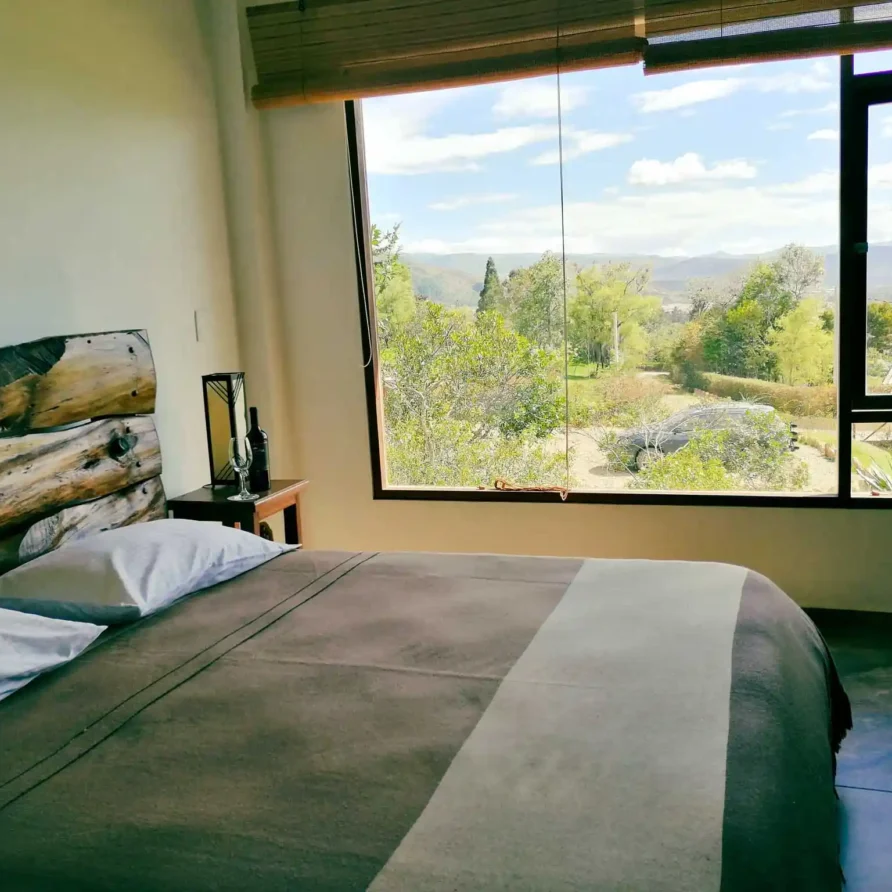 Cama doble en suite rústica de Casa Zuetana, Zipaquirá, frente a ventanal que muestra un paisaje natural amplio y sereno.
