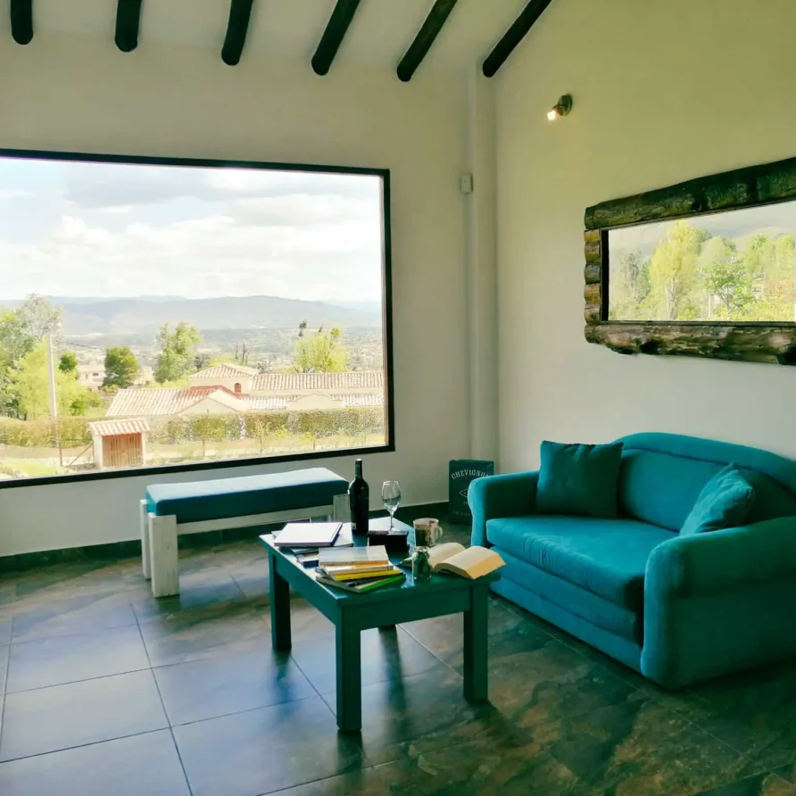 Moderna sala de Casa Zuetana en Zipaquirá con sofá turquesa y vistas panorámicas a montañas y valle.