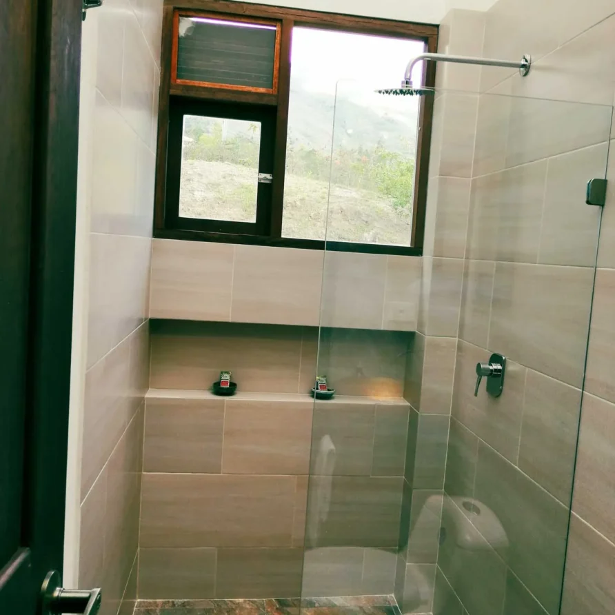 Baño moderno con ducha, inodoro y ventana con vista a la naturaleza en Casa Zuetana, alquiler vacacional en Zipaquirá.