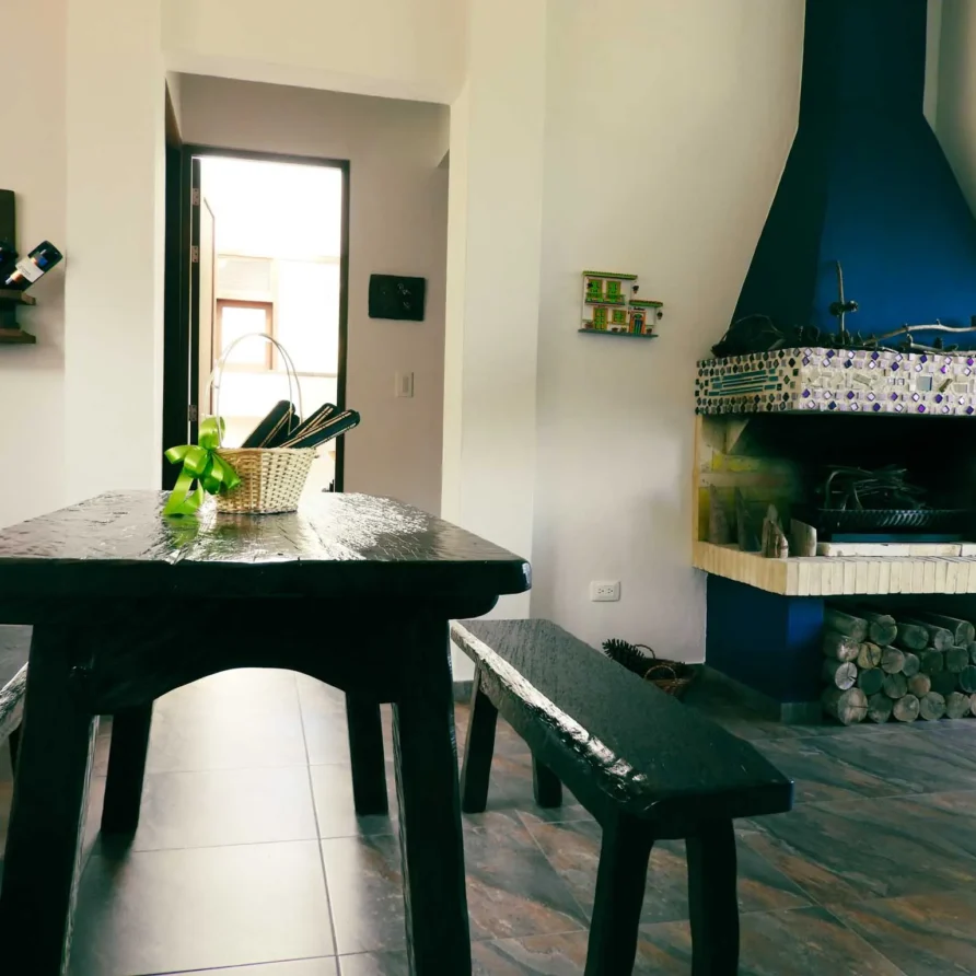 Interior de alquiler vacacional en Zipaquirá: mesa de madera, chimenea con mosaico y botelleros en la pared.