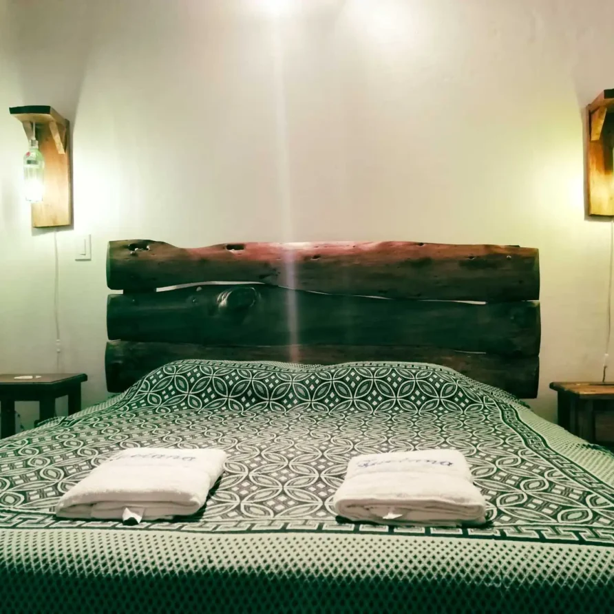 Habitación rústica en Casa Zuetana, Zipaquirá con cama doble, cabecero de madera y lámparas artesanales.