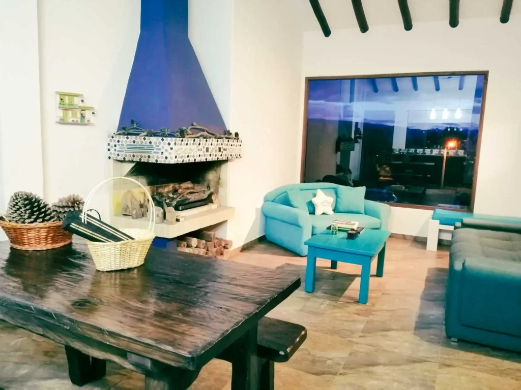 Acogedora sala de estar en Casa Zuetana, Zipaquirá, con chimenea azul, sofás turquesa y mesa de madera rústica.