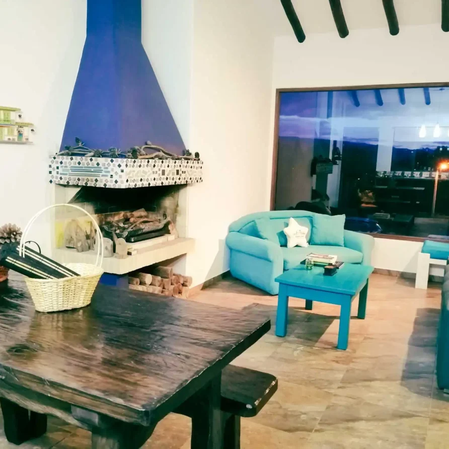 Acogedora sala de estar en Casa Zuetana, Zipaquirá, con chimenea azul, sofás turquesa y mesa de madera rústica.