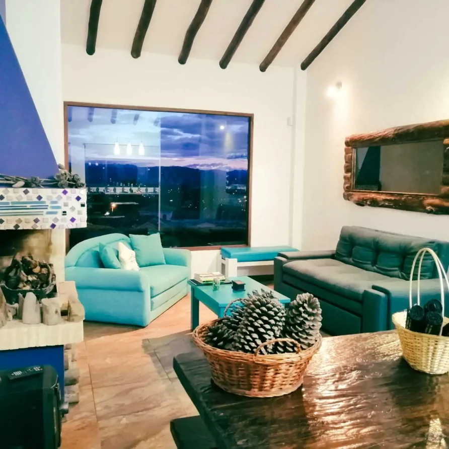 Interior de casa de alquiler vacacional en Zipaquirá con comedor de madera, chimenea y gran ventana con vistas nocturnas.