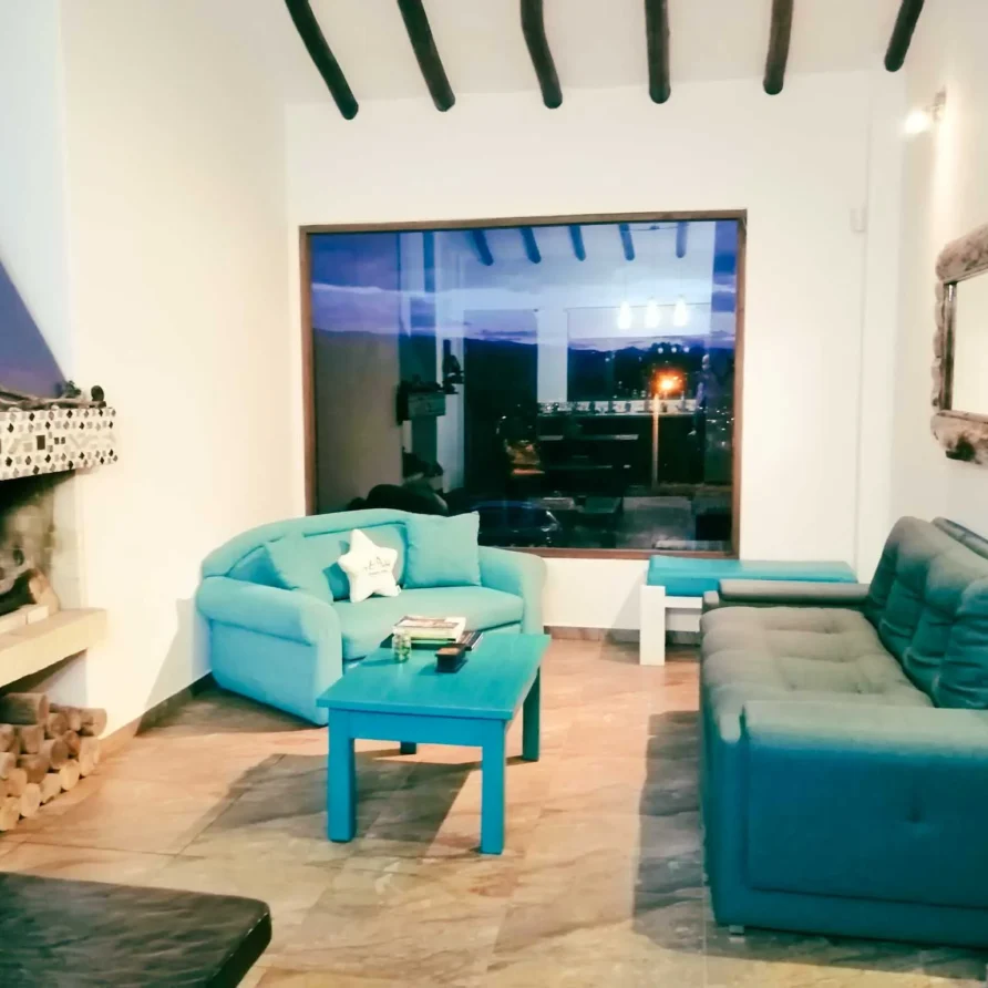 Hermosa sala de alquiler vacacional en Zipaquirá con mobiliario vibrante, grandes ventanales y leña para la chimenea.