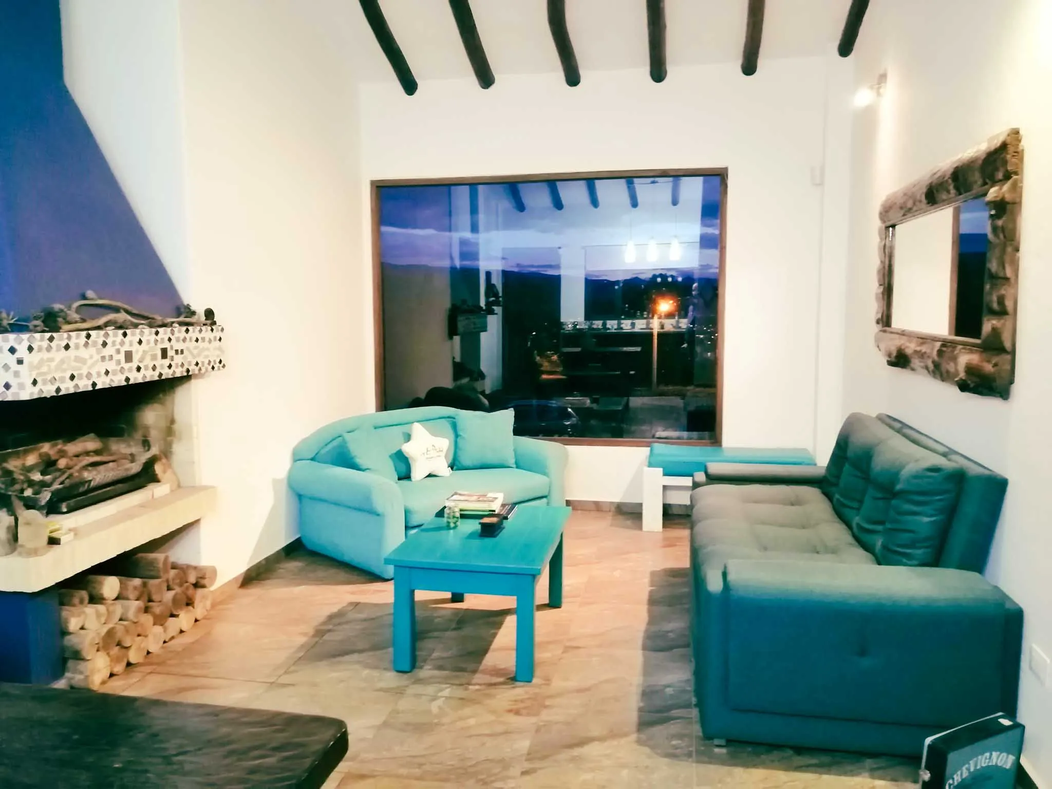 Hermosa sala de alquiler vacacional en Zipaquirá con mobiliario vibrante, grandes ventanales y leña para la chimenea.
