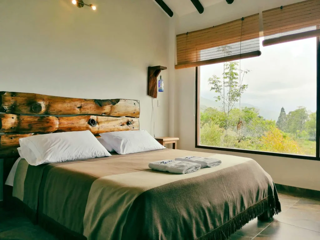 Habitación rústica de Casa Zuetana en Zipaquira, con cama y cabecero de troncos, y gran ventana con vista natural.