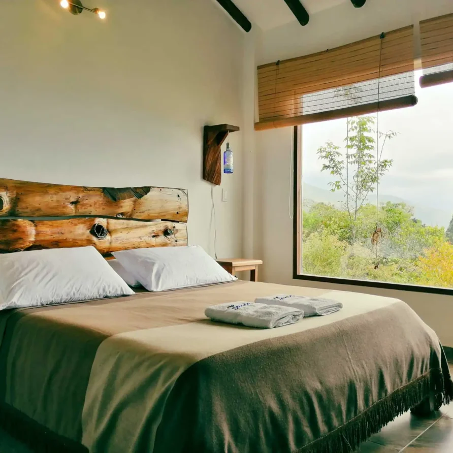 Habitación rústica de Casa Zuetana en Zipaquira, con cama y cabecero de troncos, y gran ventana con vista natural.