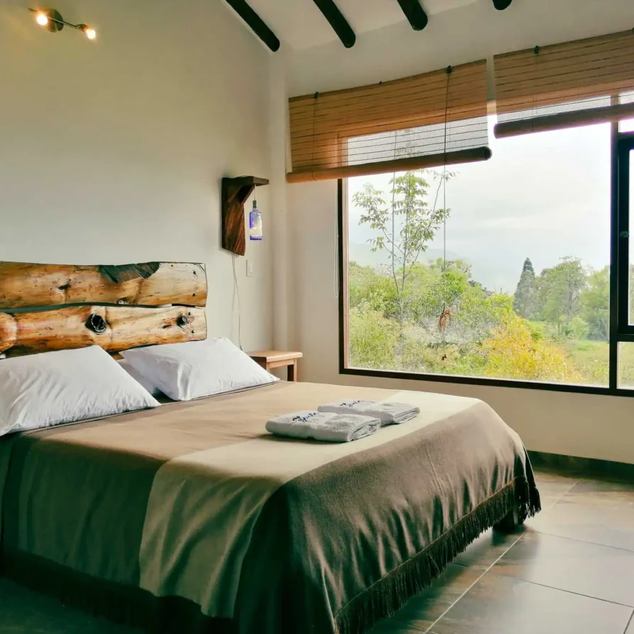 Habitación rústica de Casa Zuetana en Zipaquira, con cama y cabecero de troncos, y gran ventana con vista natural.