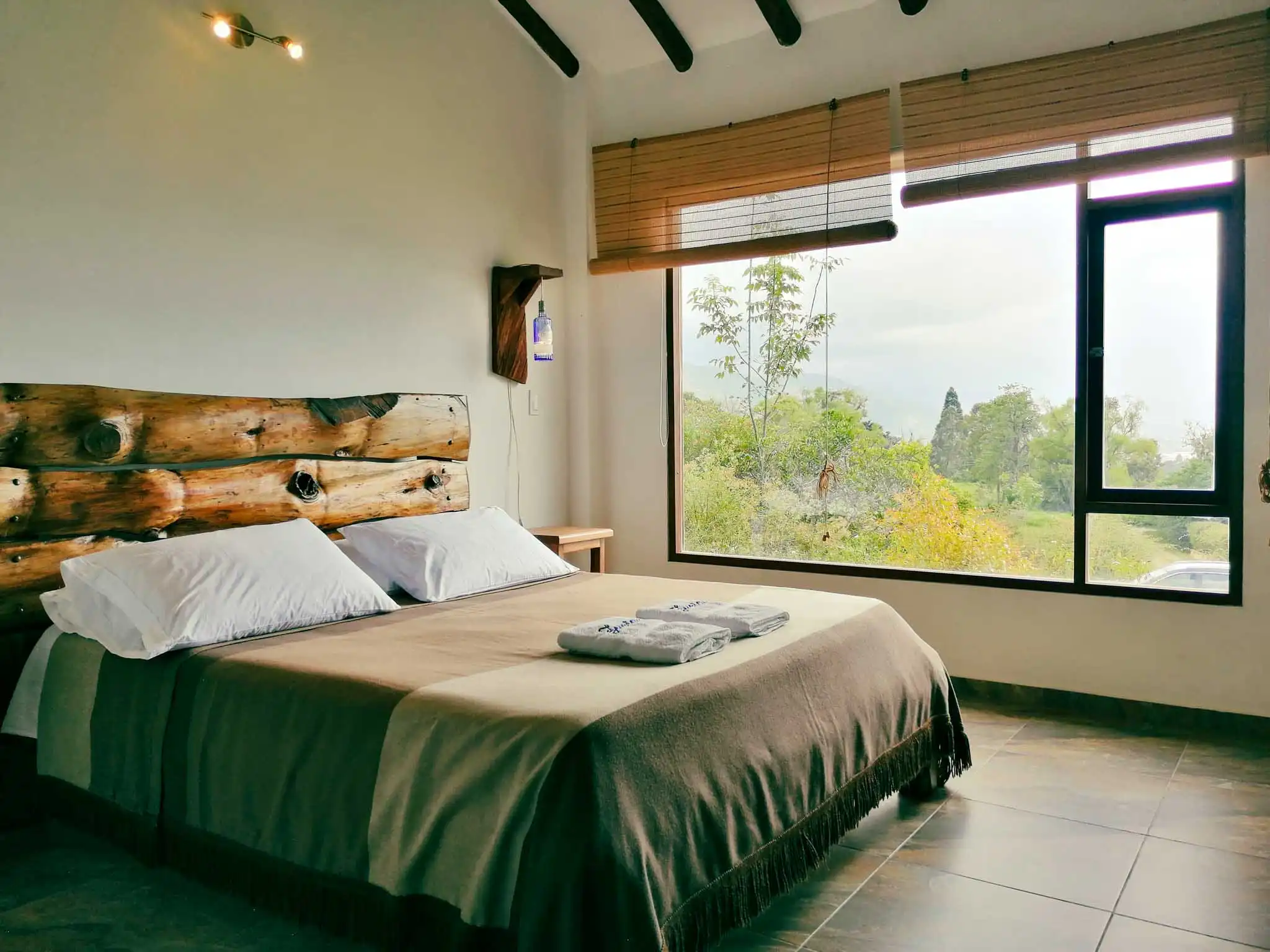 Habitación rústica de Casa Zuetana en Zipaquira, con cama y cabecero de troncos, y gran ventana con vista natural.