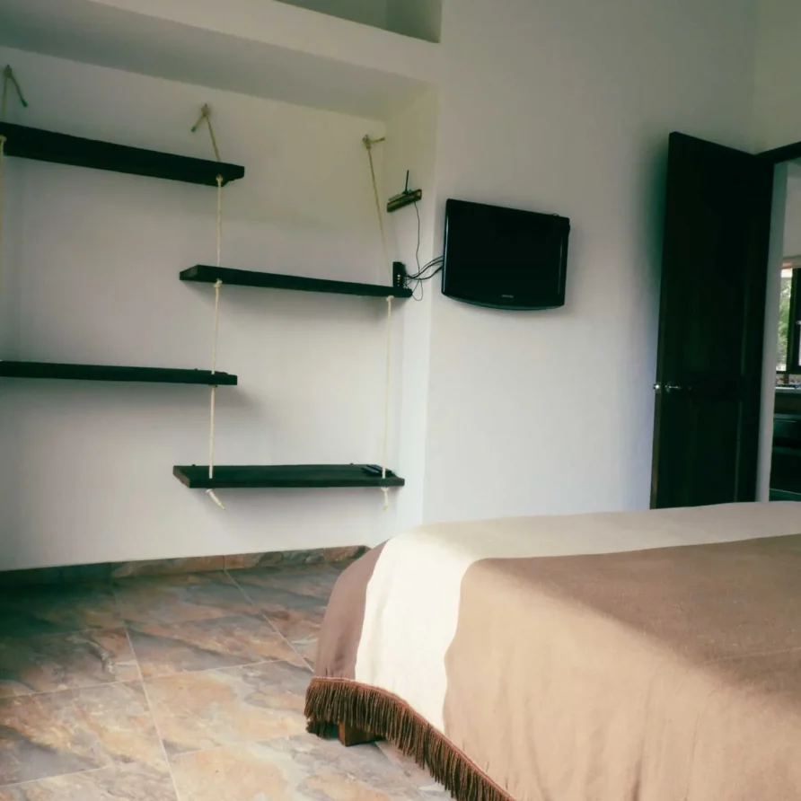 Dormitorio de Casa Zuetana en Zipaquirá con cama, estanterías rústicas colgantes y TV, ideal para alquiler vacacional.