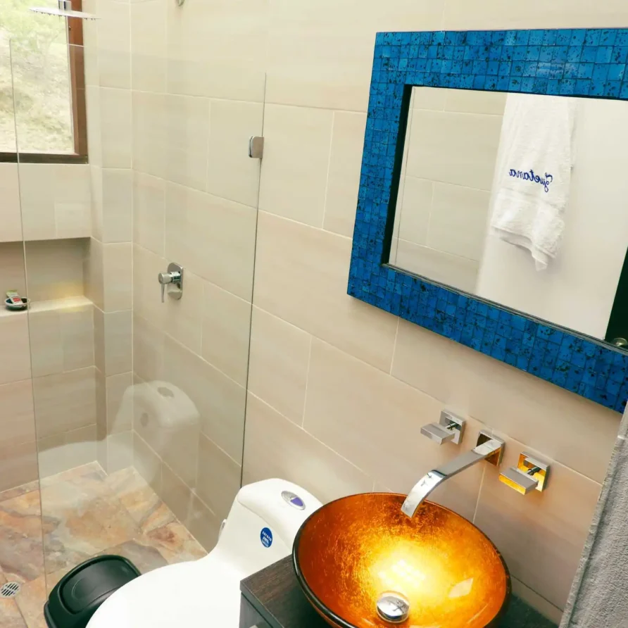Baño moderno en Casa Zuetana Zipaquirá con ducha de cristal, lavabo de diseño y espejo azul decorativo.