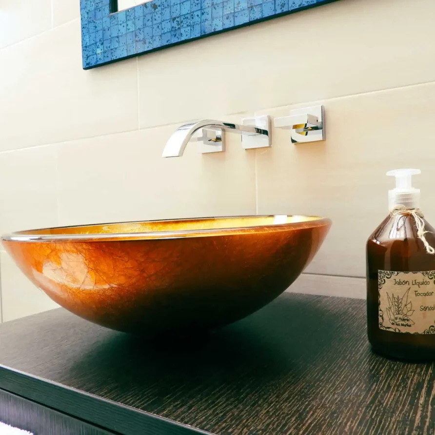 Moderno lavabo de cristal ámbar y grifo cromado en baño de Casa Zuetana, Zipaquirá. Ideal para alquiler vacacional.