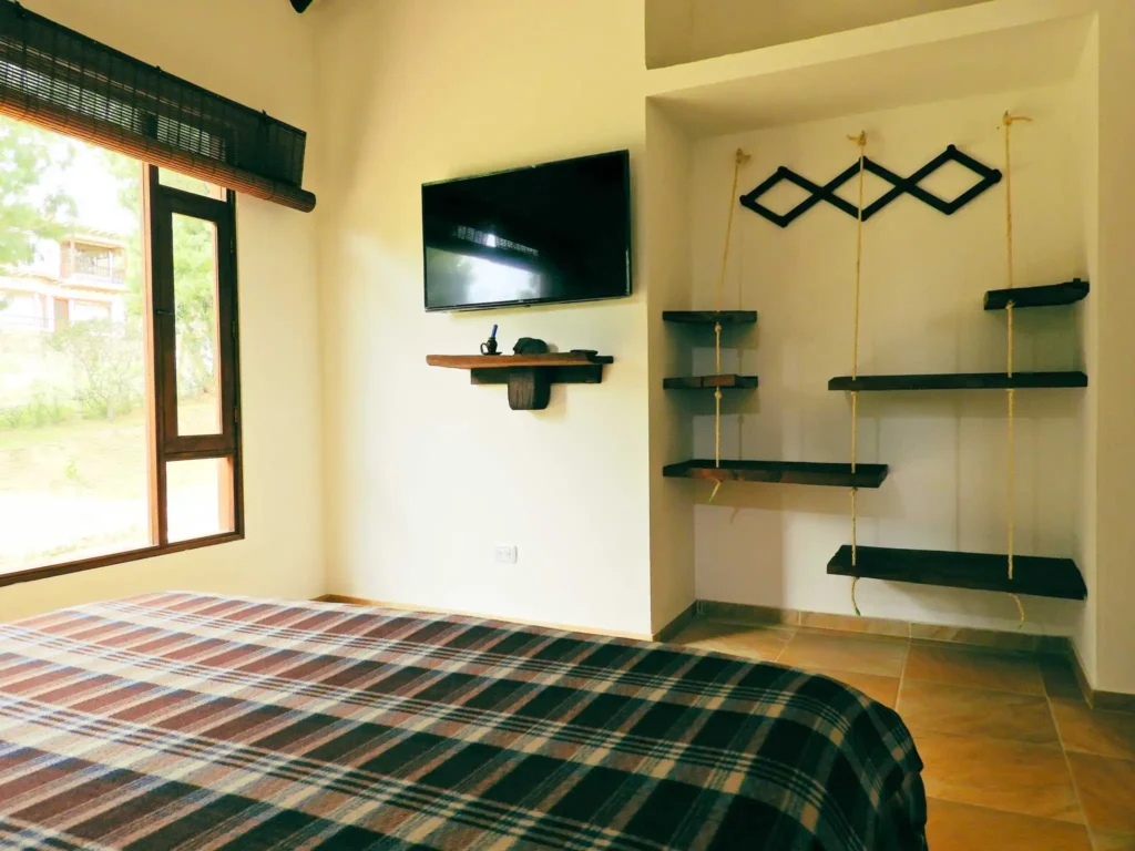 Acogedora habitación de alquiler vacacional en Zipaquirá con manta a cuadros, televisión y persianas de bambú.