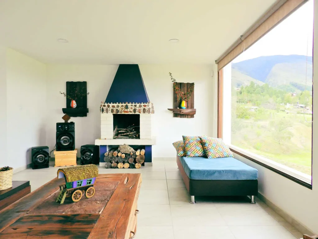 Sala acogedora en Casa Hichatana, Zipaquirá, con chimenea de piedra, vista a la montaña y sofá. Ideal alquiler vacacional.