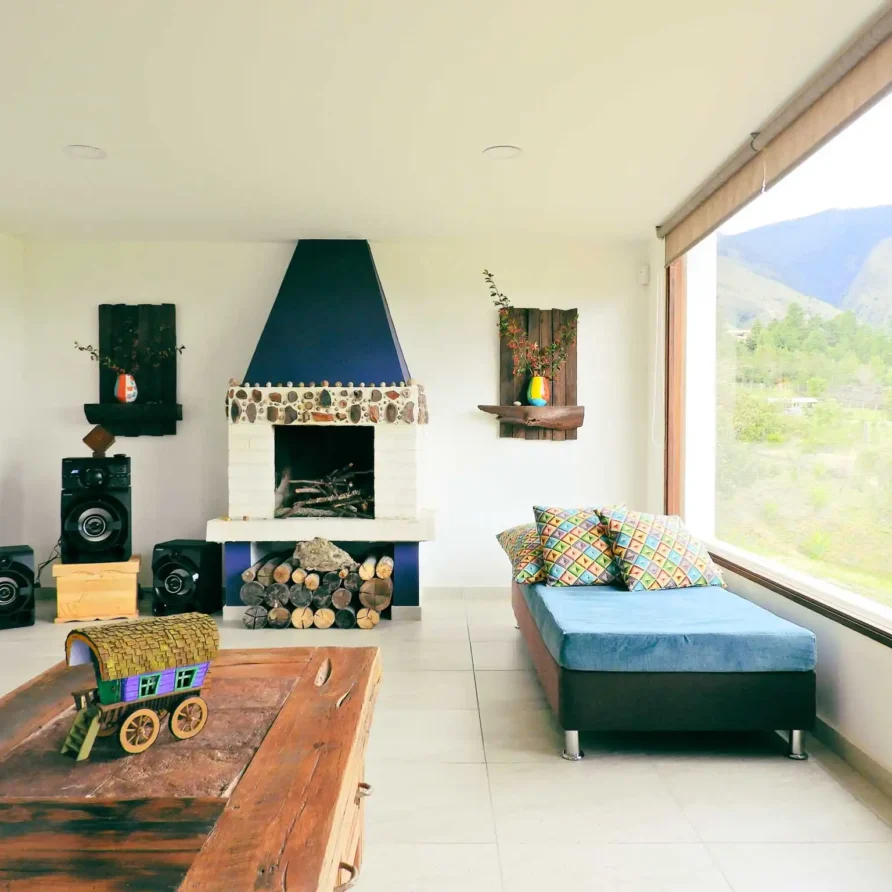 Sala acogedora en Casa Hichatana, Zipaquirá, con chimenea de piedra, vista a la montaña y sofá. Ideal alquiler vacacional.