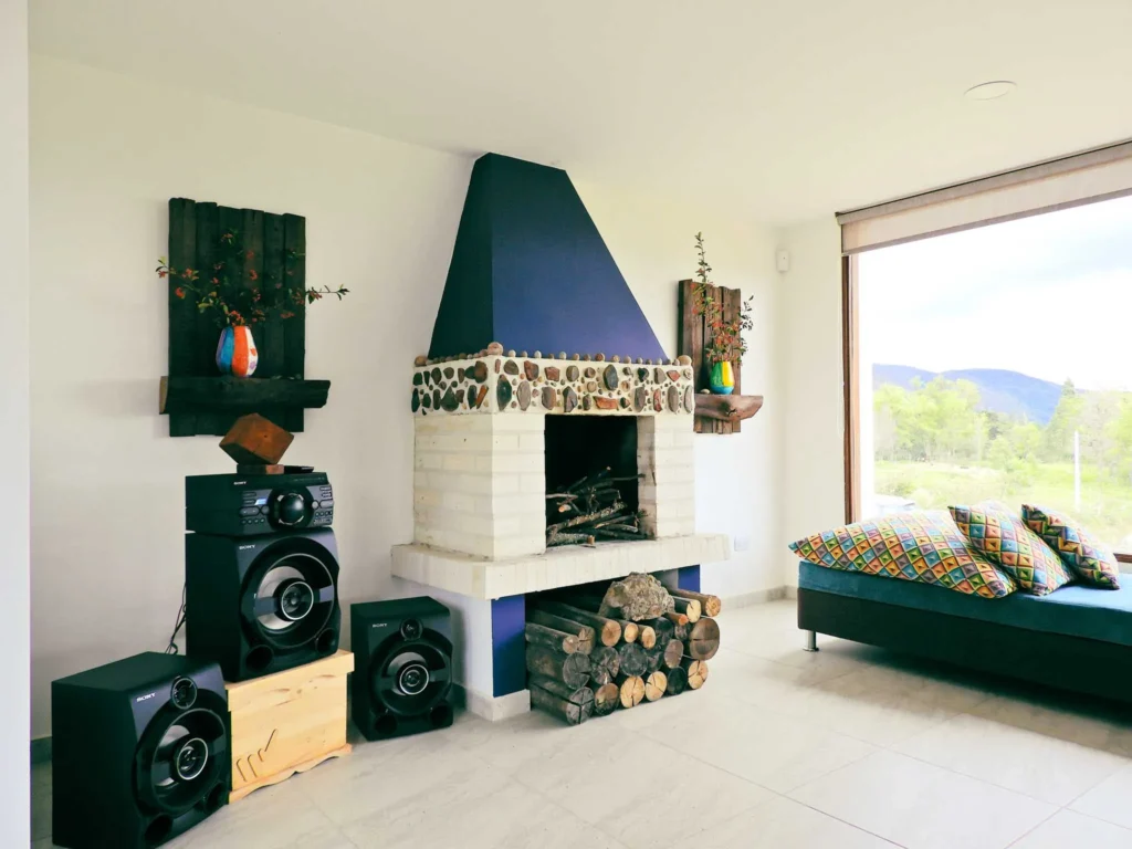 Acogedora sala de Casa Hichatana en Zipaquirá con chimenea de piedra, sofá colorido, sistema de sonido y vistas naturales.