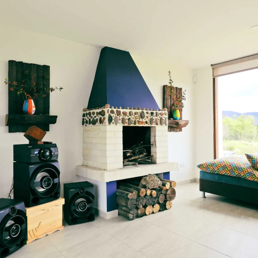 Acogedora sala de Casa Hichatana en Zipaquirá con chimenea de piedra, sofá colorido, sistema de sonido y vistas naturales.