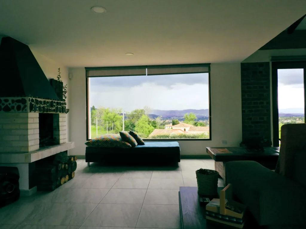 Sala de estar en Casa Hichatana, Zipaquirá, con chimenea, sofá y gran ventanal ofreciendo vistas panorámicas al paisaje.
