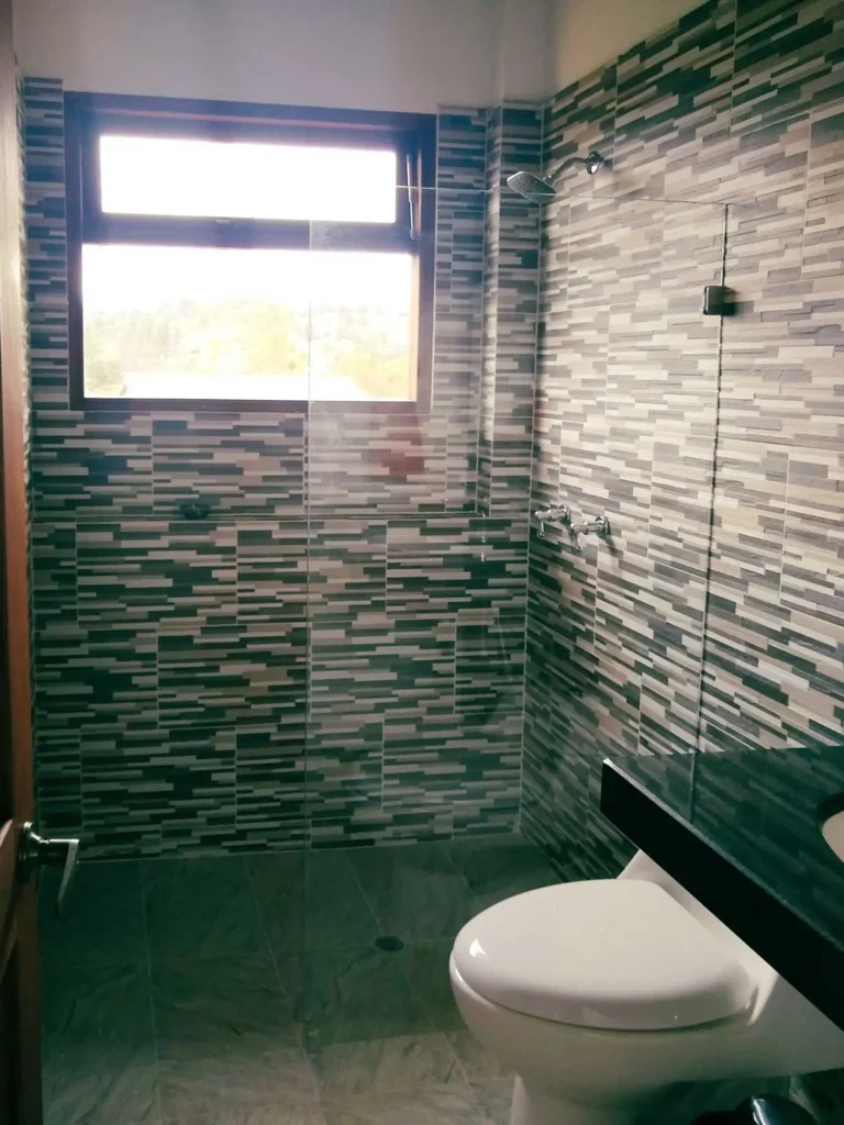 Baño moderno con azulejos de mosaico, ducha, inodoro y ventana. Parte de casa de alquiler en Zipaquirá.