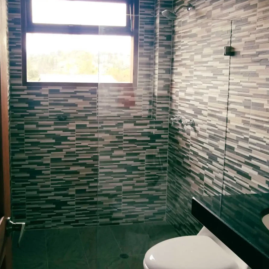 Baño moderno con azulejos de mosaico, ducha, inodoro y ventana. Parte de casa de alquiler en Zipaquirá.
