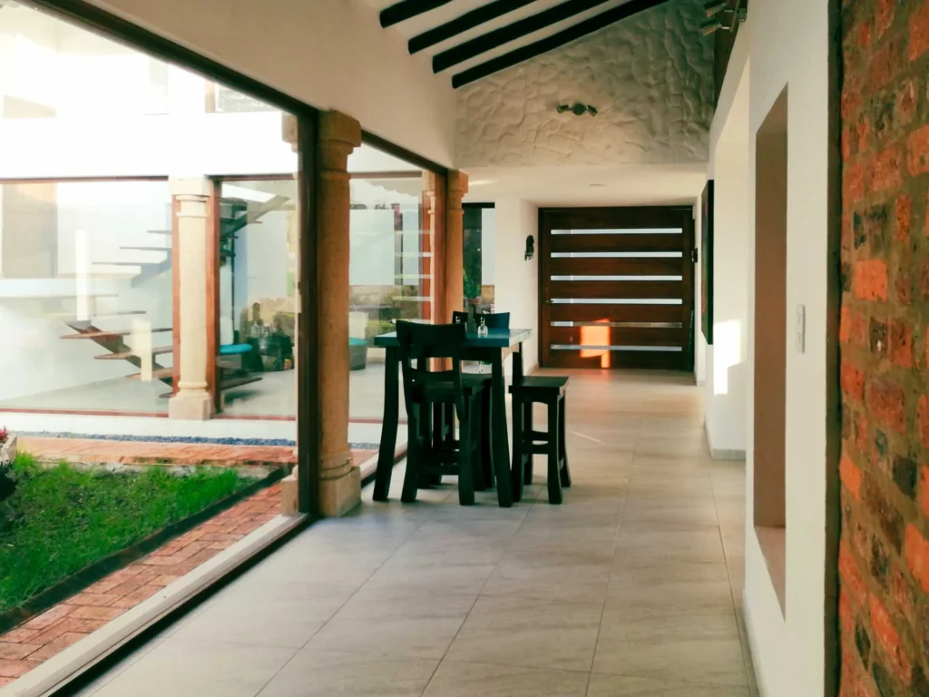Pasillo moderno de Casa Hichatana en Zipaquirá con ventanales al jardín, mesa alta y escaleras de madera.