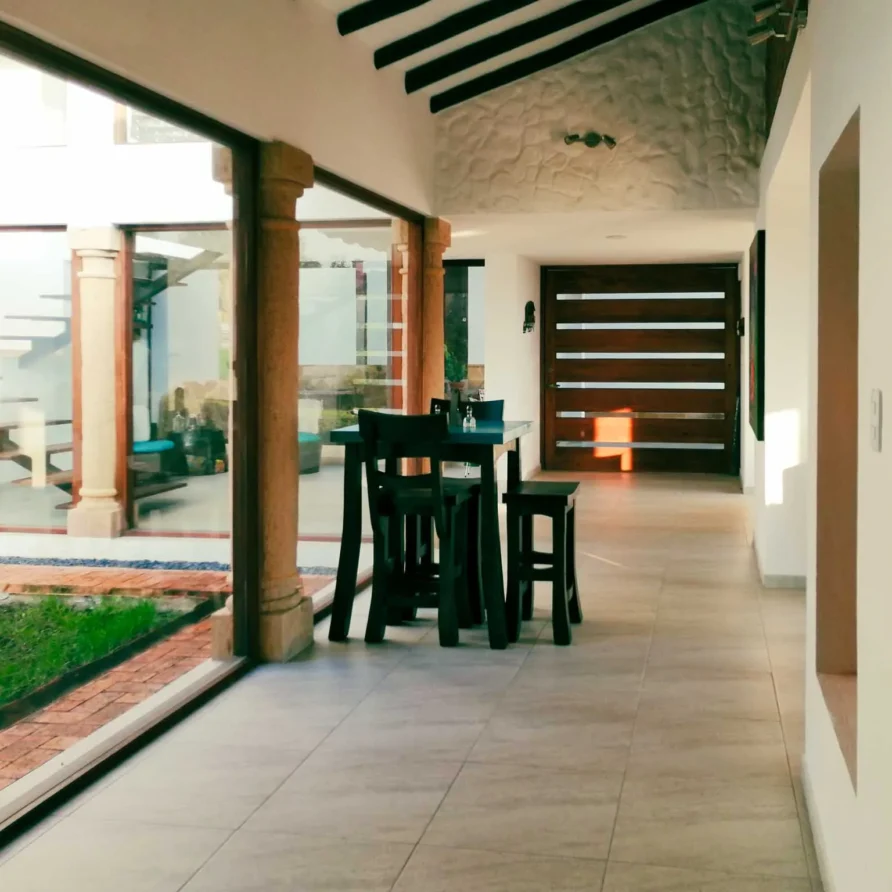Pasillo moderno de Casa Hichatana en Zipaquirá con ventanales al jardín, mesa alta y escaleras de madera.