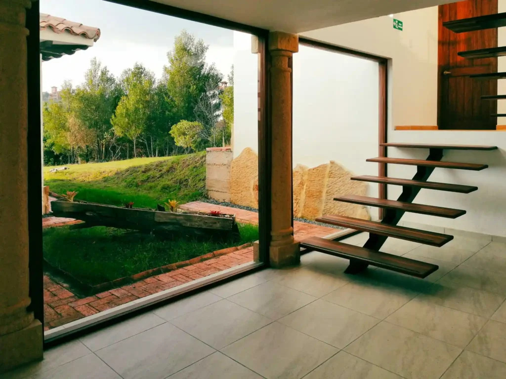 Interior luminoso de Casa Hichatana Zipaquirá con vista al jardín y moderna escalera flotante de madera.
