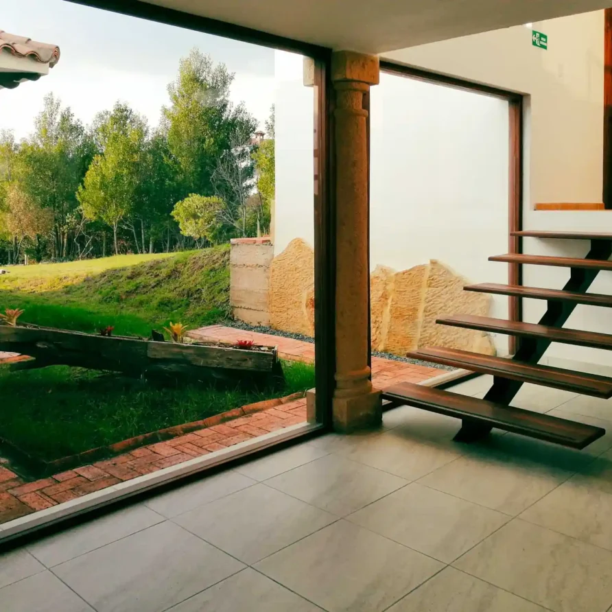 Interior luminoso de Casa Hichatana Zipaquirá con vista al jardín y moderna escalera flotante de madera.