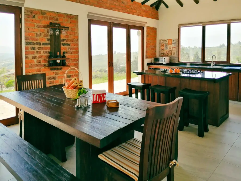 Comedor y cocina rústica de Casa Hichatana en Zipaquirá, con mesa de madera, ladrillo visto y vistas al paisaje.