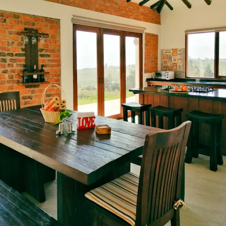 Comedor y cocina rústica de Casa Hichatana en Zipaquirá, con mesa de madera, ladrillo visto y vistas al paisaje.