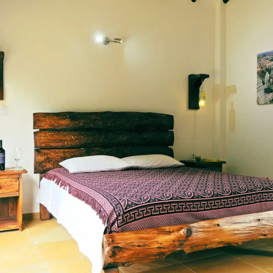 Habitación rústica en Casa Hichatana Zipaquira con cama de madera, manta decorativa y lámparas de botella.