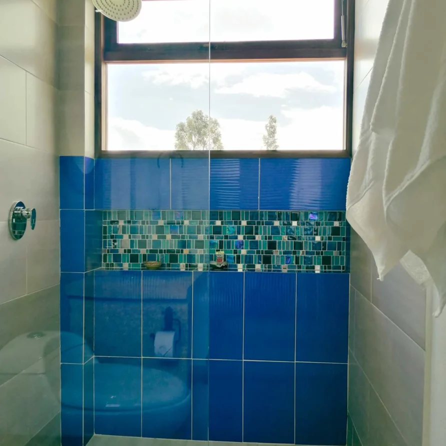 Ducha moderna con azulejos azules y mosaico en el baño de Casa Hichatana, alojamiento de alquiler en Zipaquirá.