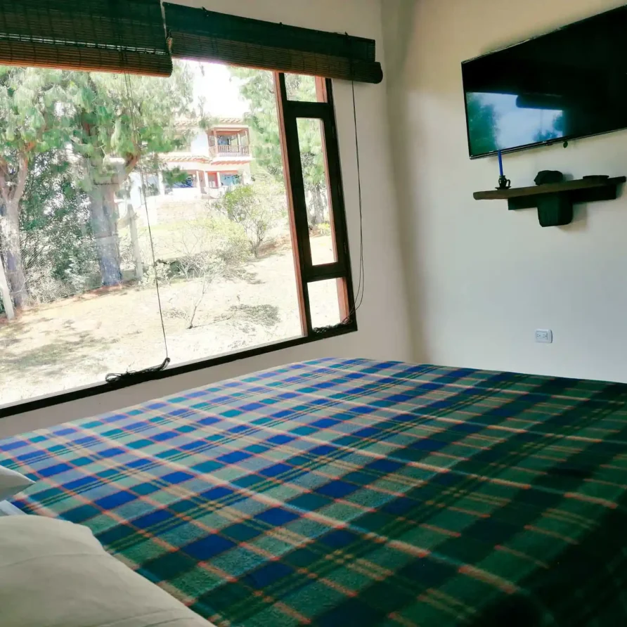 Dormitorio luminoso en Casa Hichatana, Zipaquirá, con cama, TV y vista a jardín y naturaleza, ideal para alquiler vacacional.