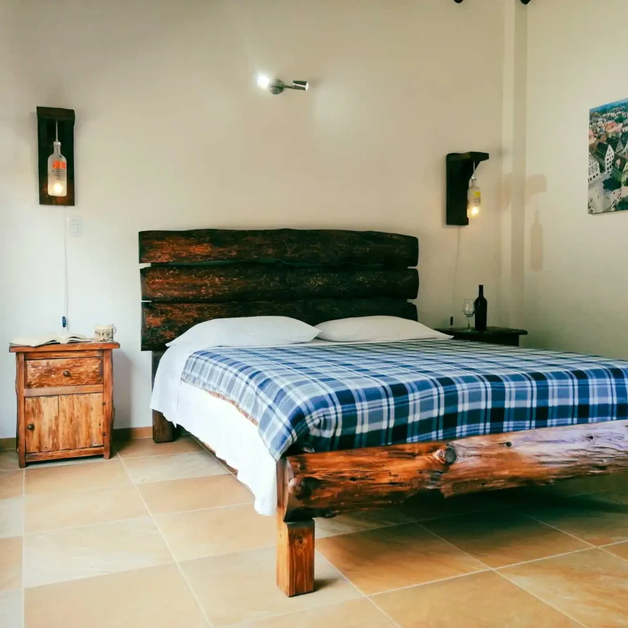 Habitación rústica con cama de madera, cabecero de troncos y manta a cuadros azul en Casa Hichatana, Zipaquirá.