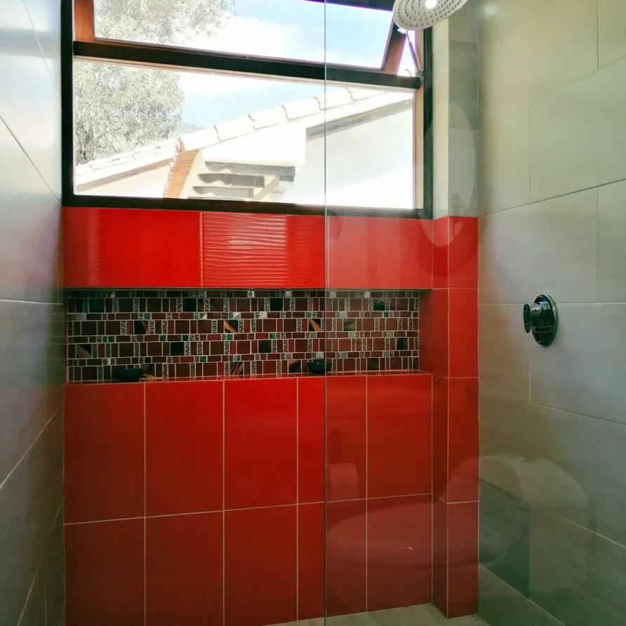 Ducha moderna con azulejos rojos, mosaico y ventana en Casa Hichatana Zipaquirá, ideal para alquiler vacacional.