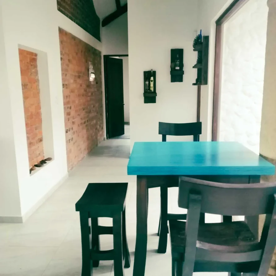 Interior de Casa Hichatana en Zipaquirá, con mesa turquesa, sillas de madera oscura y pared de ladrillo visto.