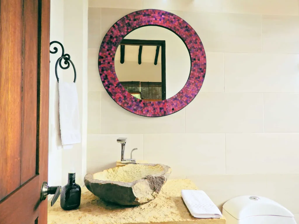 Baño de diseño en Casa Hichatana, Zipaquira: lavabo de piedra, espejo con marco mosaico y toallero de forja.