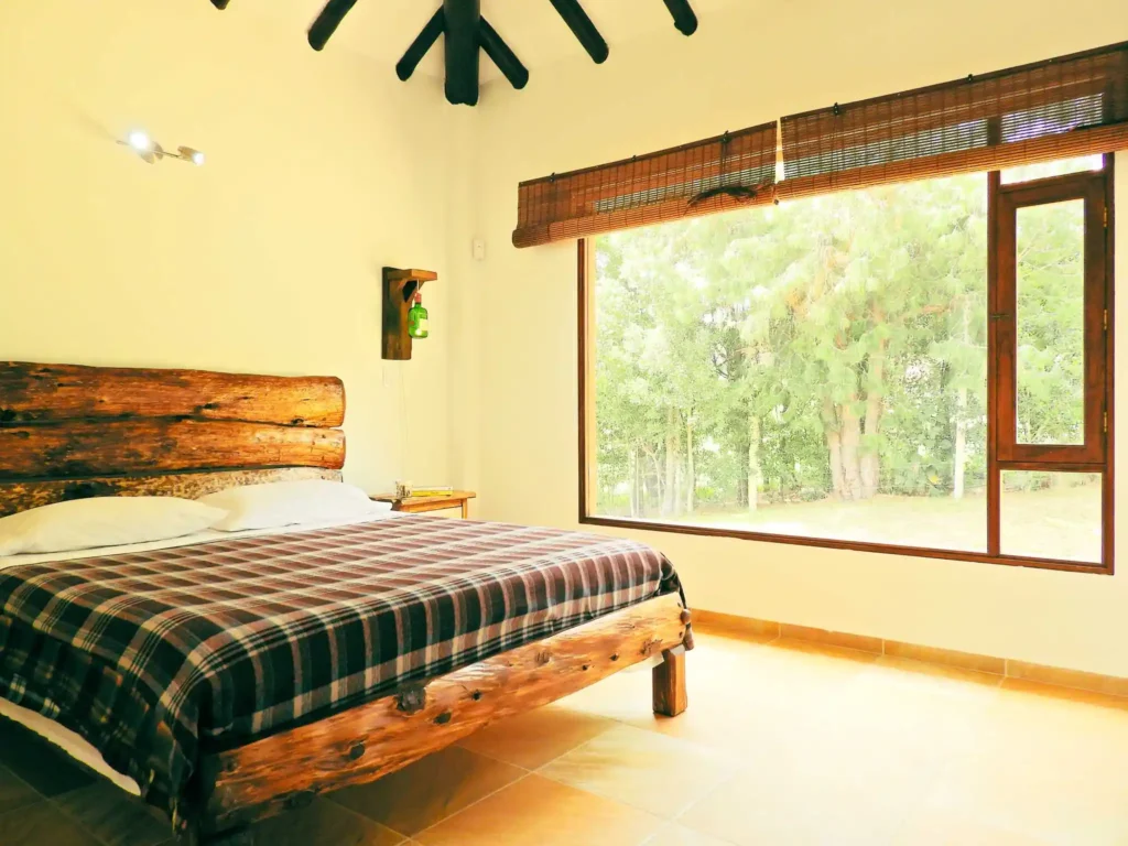 Dormitorio acogedor con cama de tronco de madera y gran ventanal en Casa Hichatana, cerca de la Catedral de Sal de Zipaquirá.