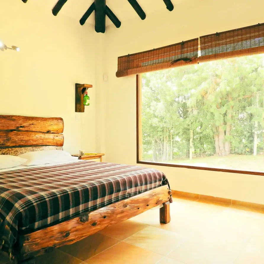 Dormitorio acogedor con cama de tronco de madera y gran ventanal en Casa Hichatana, cerca de la Catedral de Sal de Zipaquirá.
