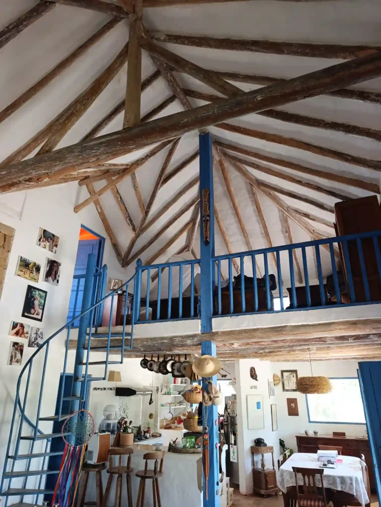 Interior de Cabaña El Ensueño en Villa de Leyva con techo de vigas de madera, escalera de caracol azul y mezzanine.