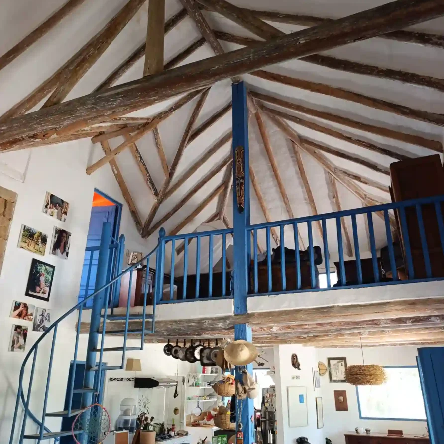 Interior de Cabaña El Ensueño en Villa de Leyva con techo de vigas de madera, escalera de caracol azul y mezzanine.