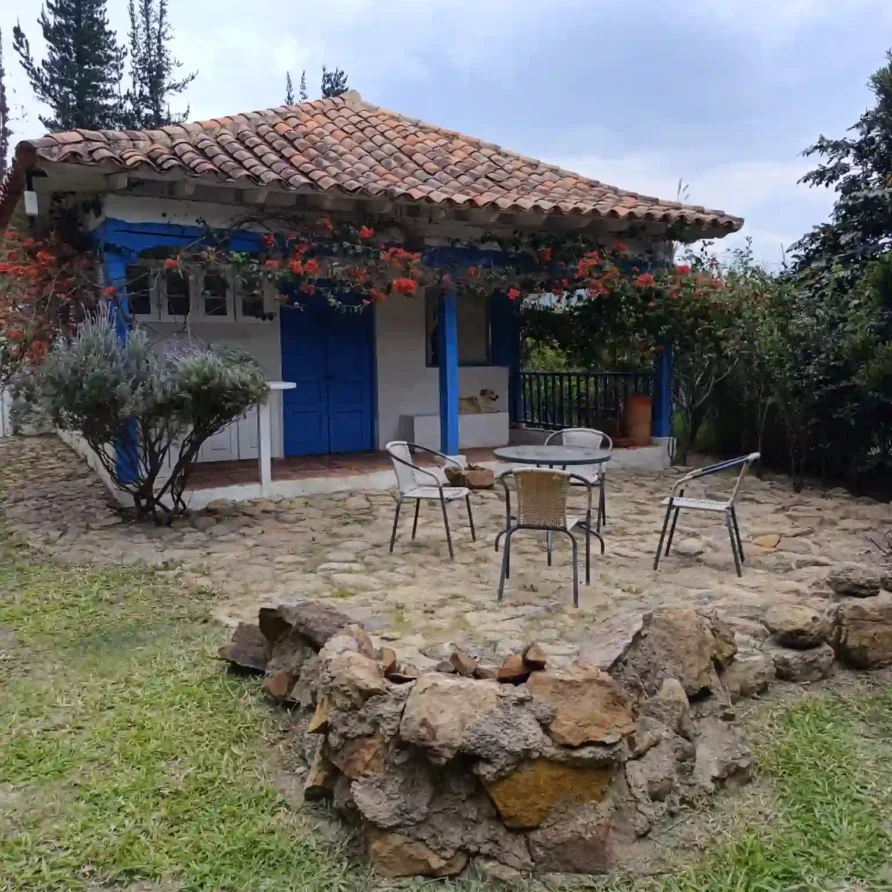 Vista de la Cabaña El Oteo, Villa de Leyva, fachada azul y blanca, tejado colonial, fogón de piedra.