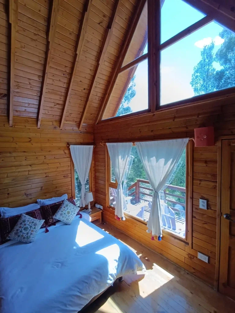 Interior de casa de campo rústica y de lujo con cama confortable, detalles de madera y balcón exterior visible. Cabaña el ensueño