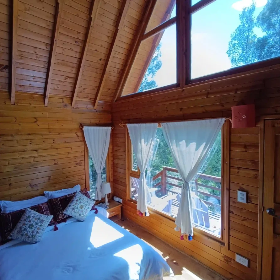 Interior de casa de campo rústica y de lujo con cama confortable, detalles de madera y balcón exterior visible. Cabaña el ensueño