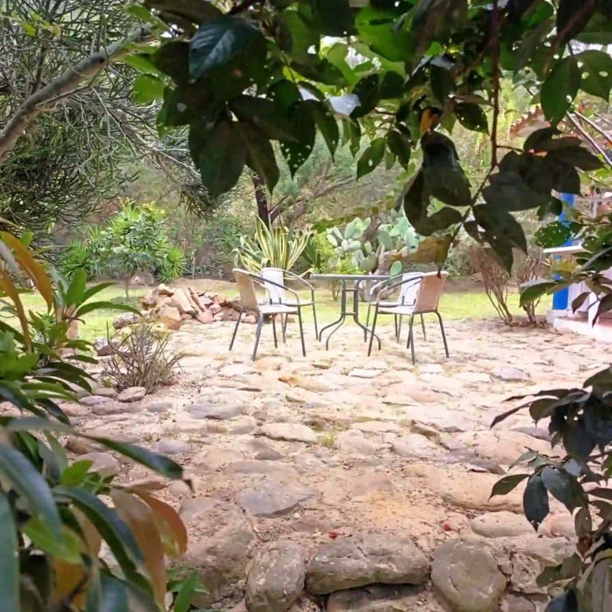 Patio de piedra con mesa y sillas de jardín, rodeado de exuberante vegetación en una cabaña de Villa de Leyva.